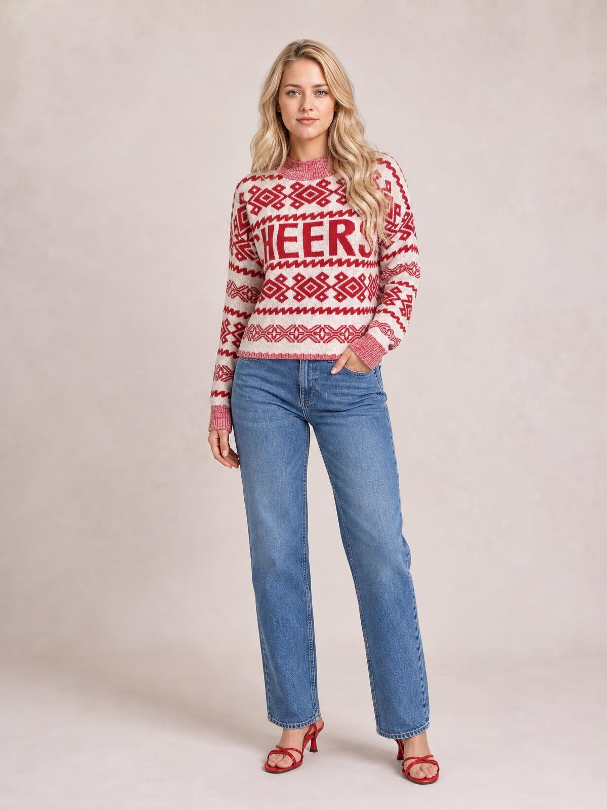 A woman poses in a red and cream Christmas sweater with a round neck, long sleeves, geometric knit patterns, and bold “CHEERS” lettering.