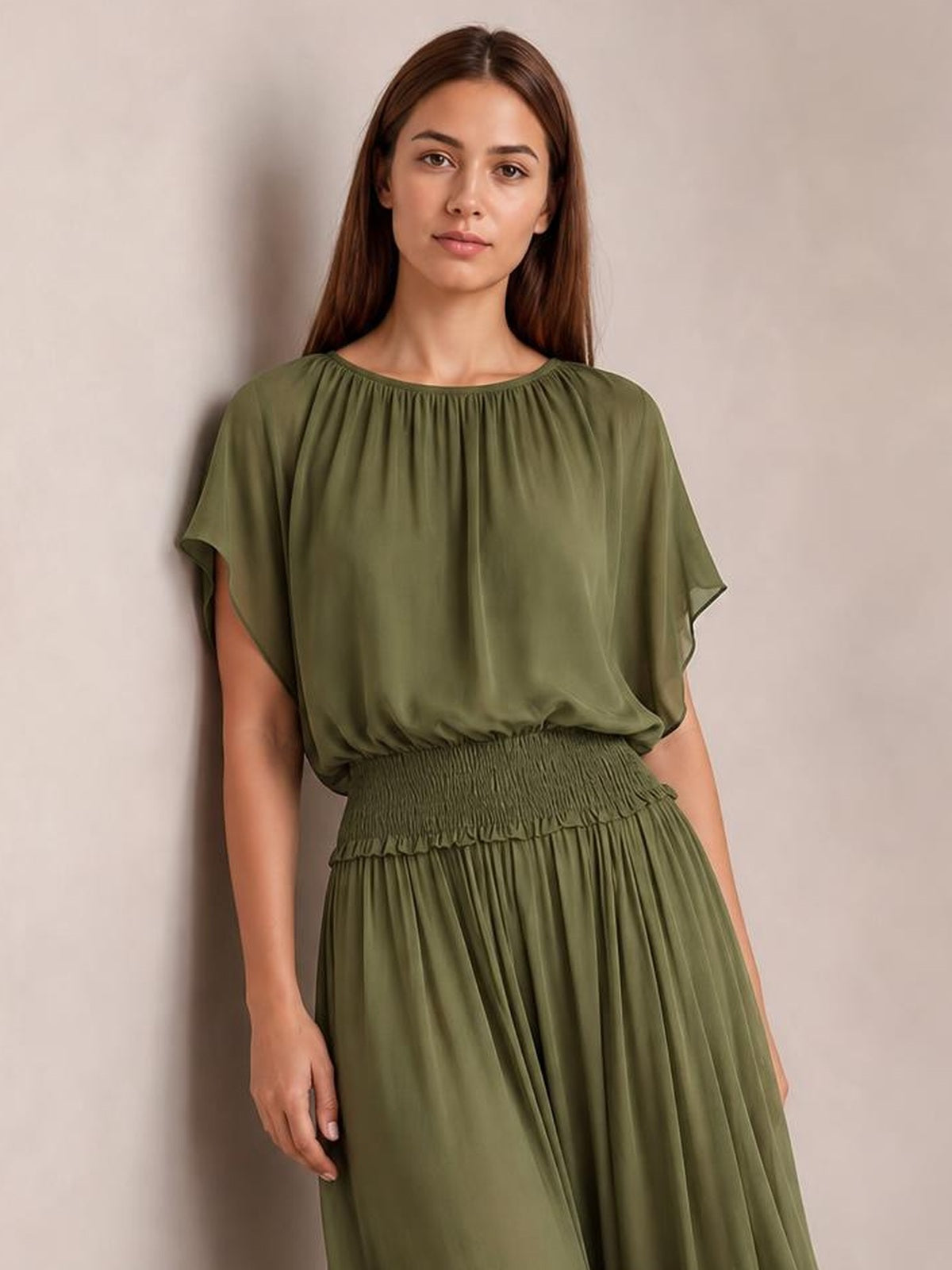 A model stands in an olive-green chiffon maxi dress with a gathered round neckline, flutter sleeves, smocked waist, and flowing full skirt.