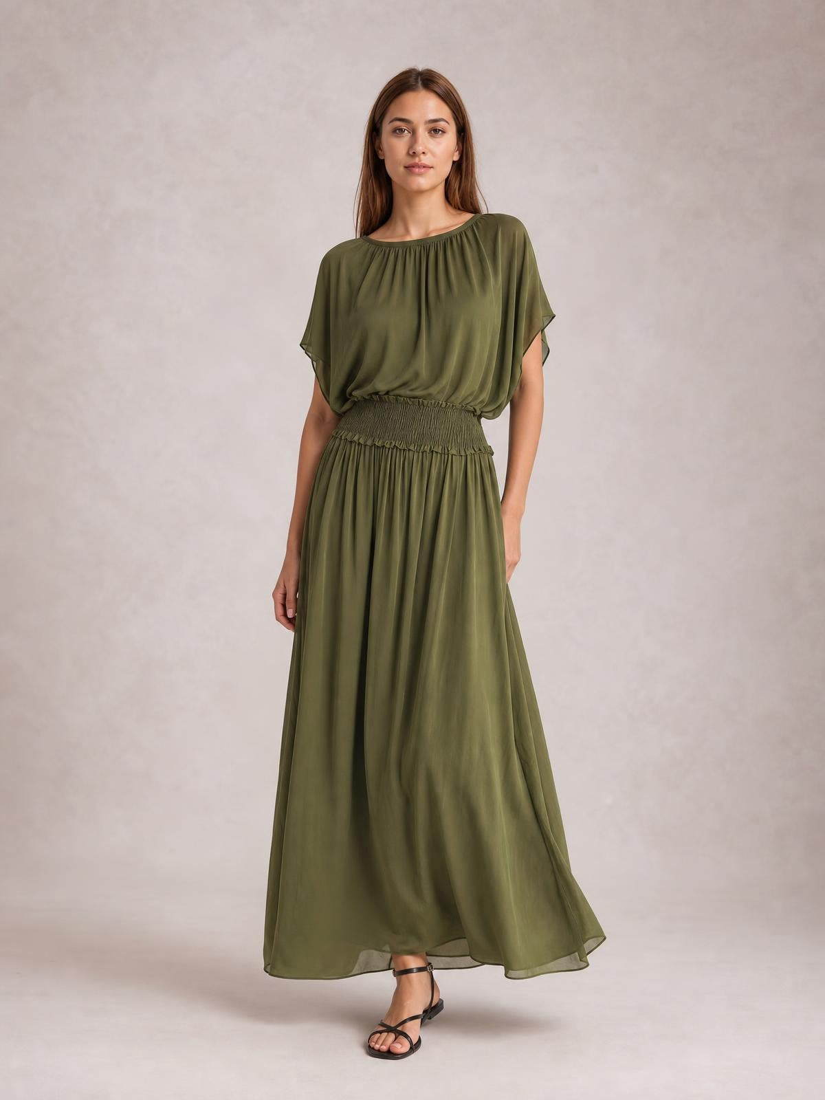 Model wears an olive green chiffon maxi dress with a smocked waist, gathered round neckline, flutter sleeves, and a flowing floor-length silhouette.