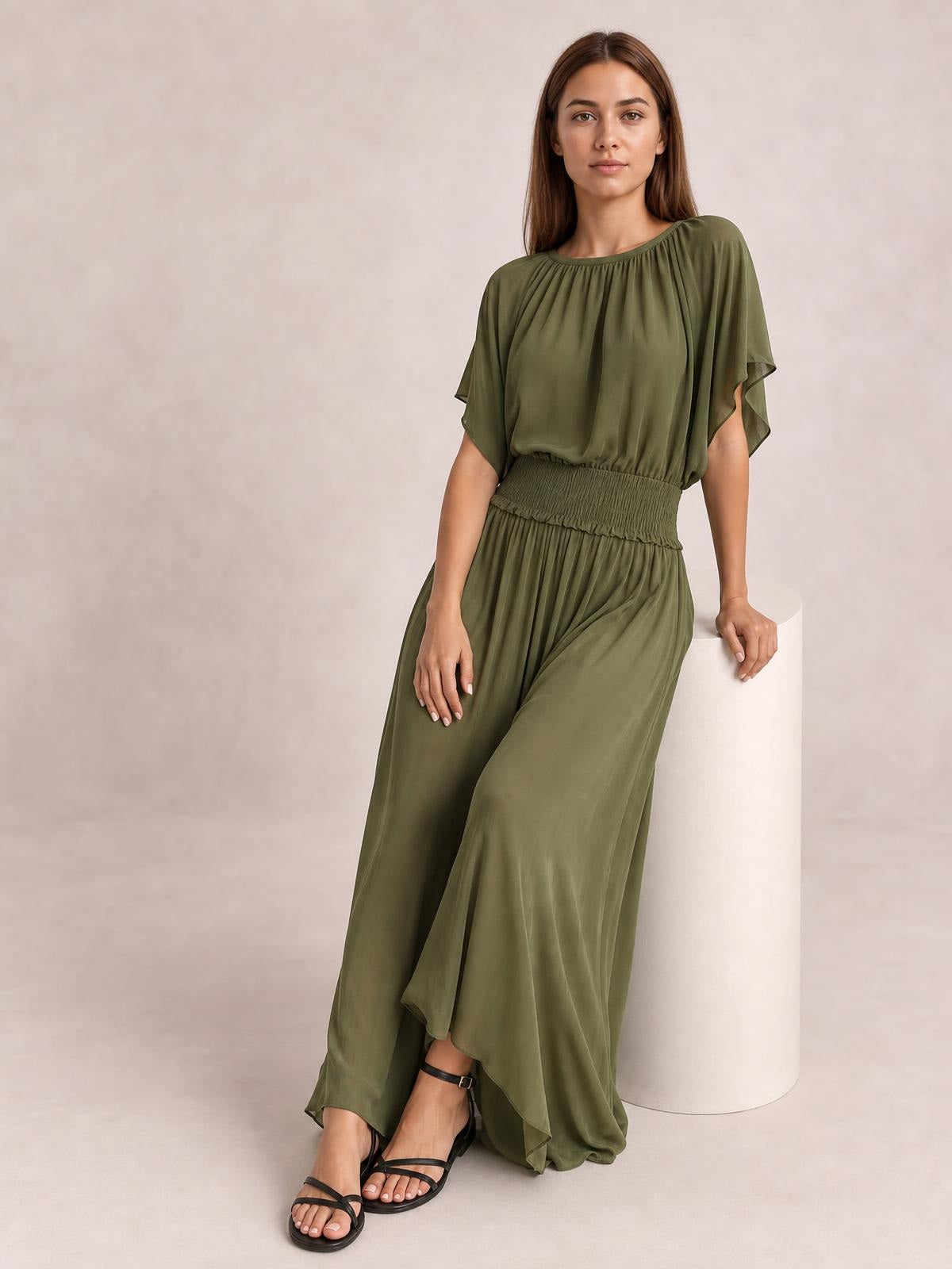 A model wears an olive chiffon maxi dress with a gathered round neckline, flutter sleeves, smocked waist, and a flowing floor-length silhouette.