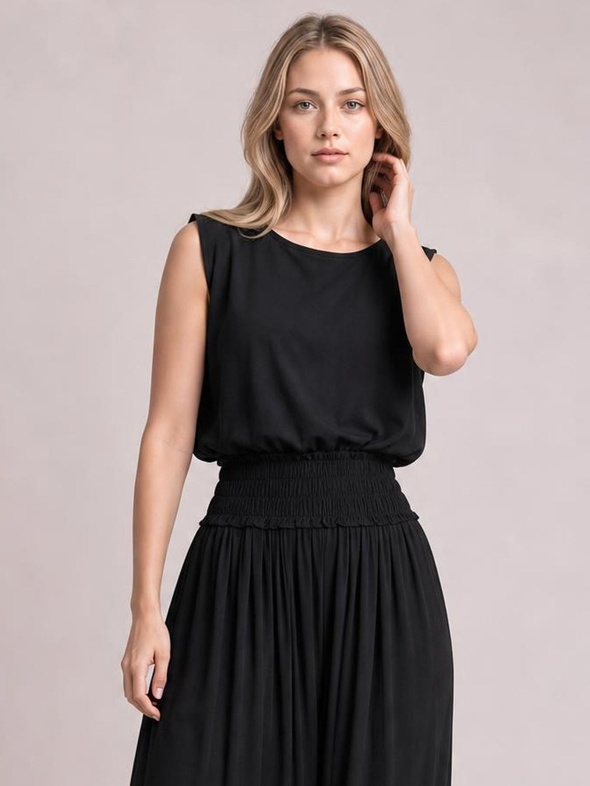A model poses in a black chiffon maxi dress with a round neckline, sleeveless silhouette, smocked waist, and softly pleated full skirt.