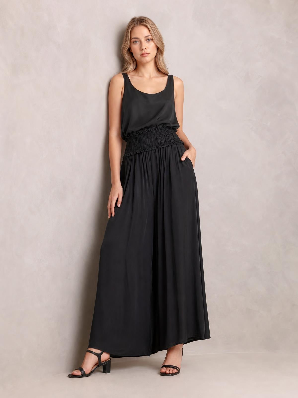 A model wears a black chiffon maxi dress with a sleeveless scoop neckline, smocked waist, flowing full-length skirt, and relaxed silhouette.