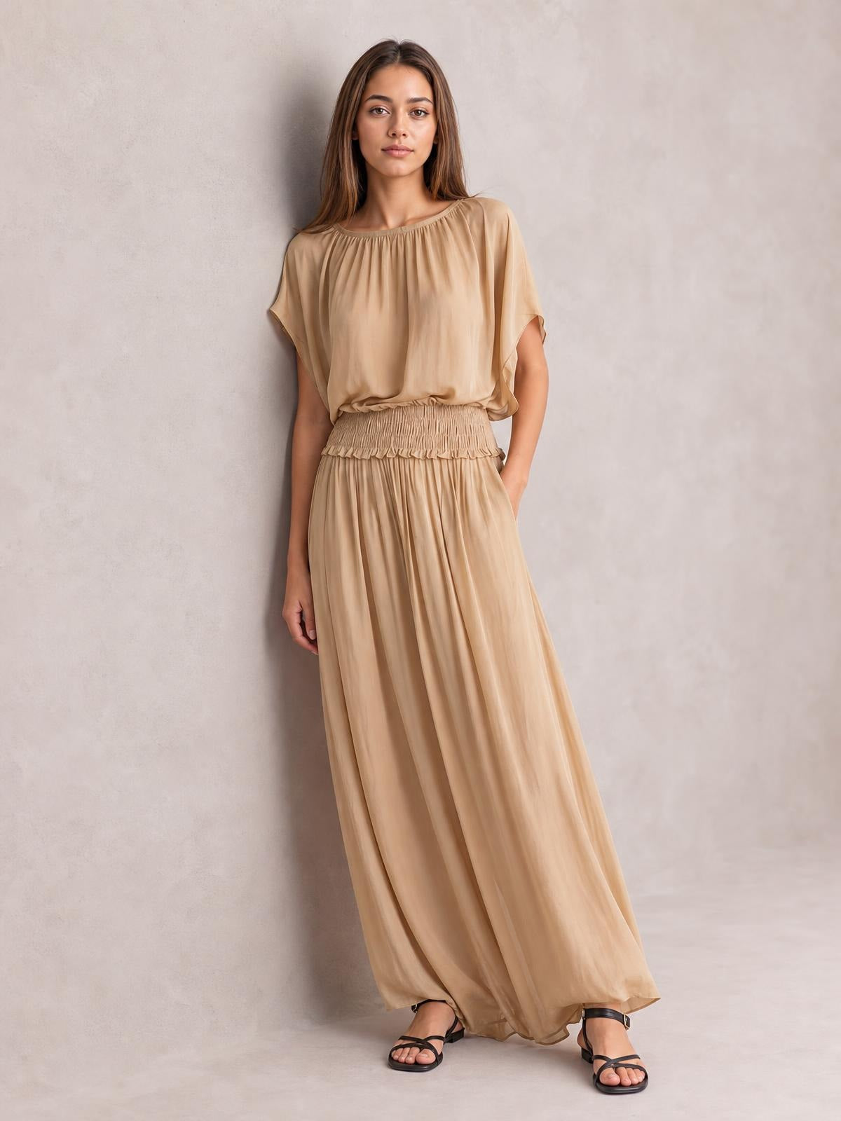 A model stands in a beige chiffon maxi dress with a smocked waist, loose gathered bodice, flutter sleeves, and a flowing floor-length silhouette.