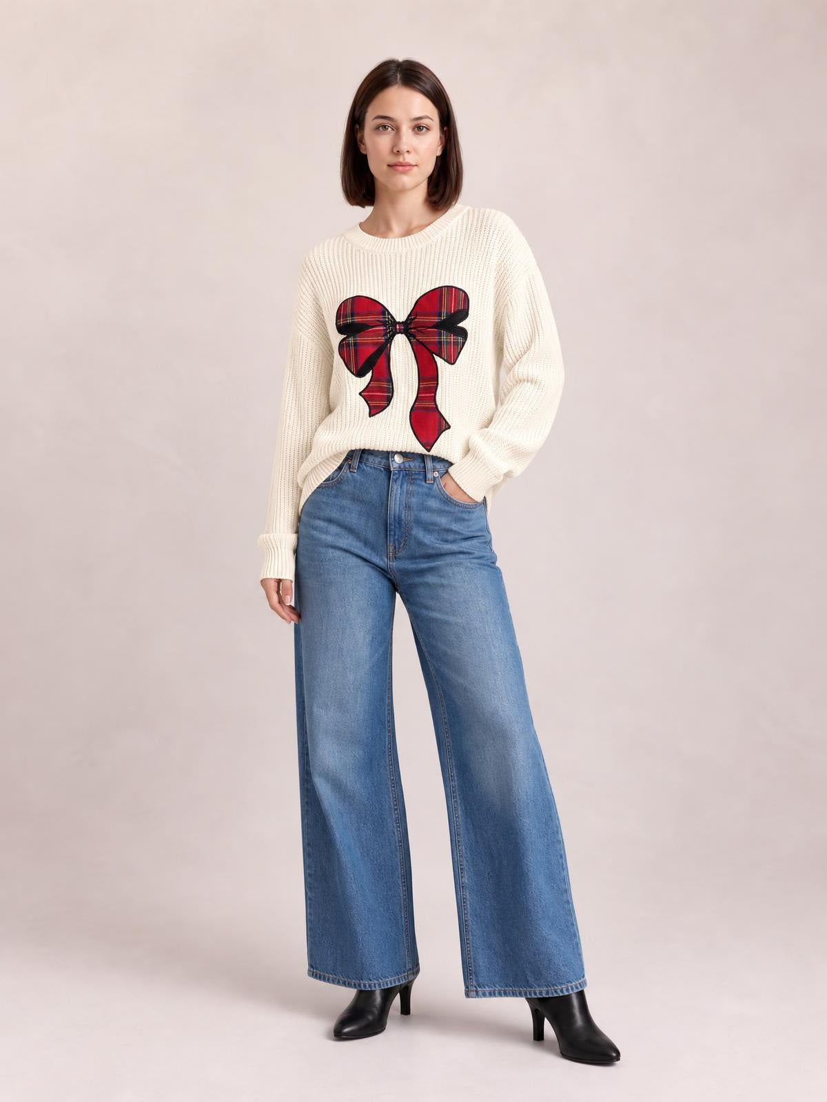 Model wears an ivory ribbed Christmas bow sweater with a relaxed dropped-shoulder silhouette, long sleeves, and a large red plaid bow on the front.