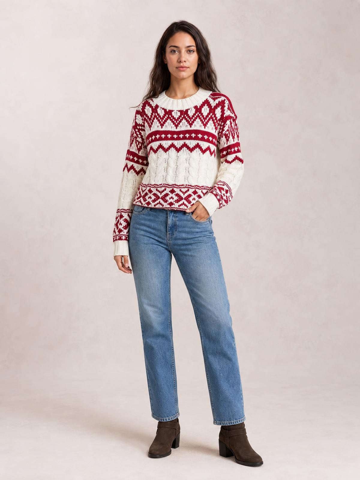Model wearing a red and white Christmas cable knit sweater with long sleeves, ribbed trim, crew neck, and a relaxed silhouette, posing with one hand in her jeans pocket.