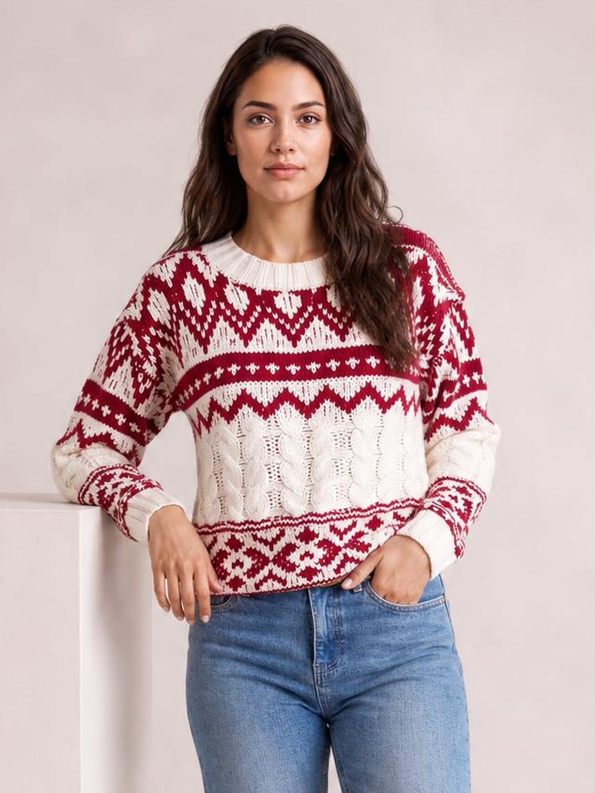 Model wears a red and white Christmas cable knit sweater with long sleeves, ribbed crew neck and cuffs, patterned relaxed silhouette, and textured knit panels.