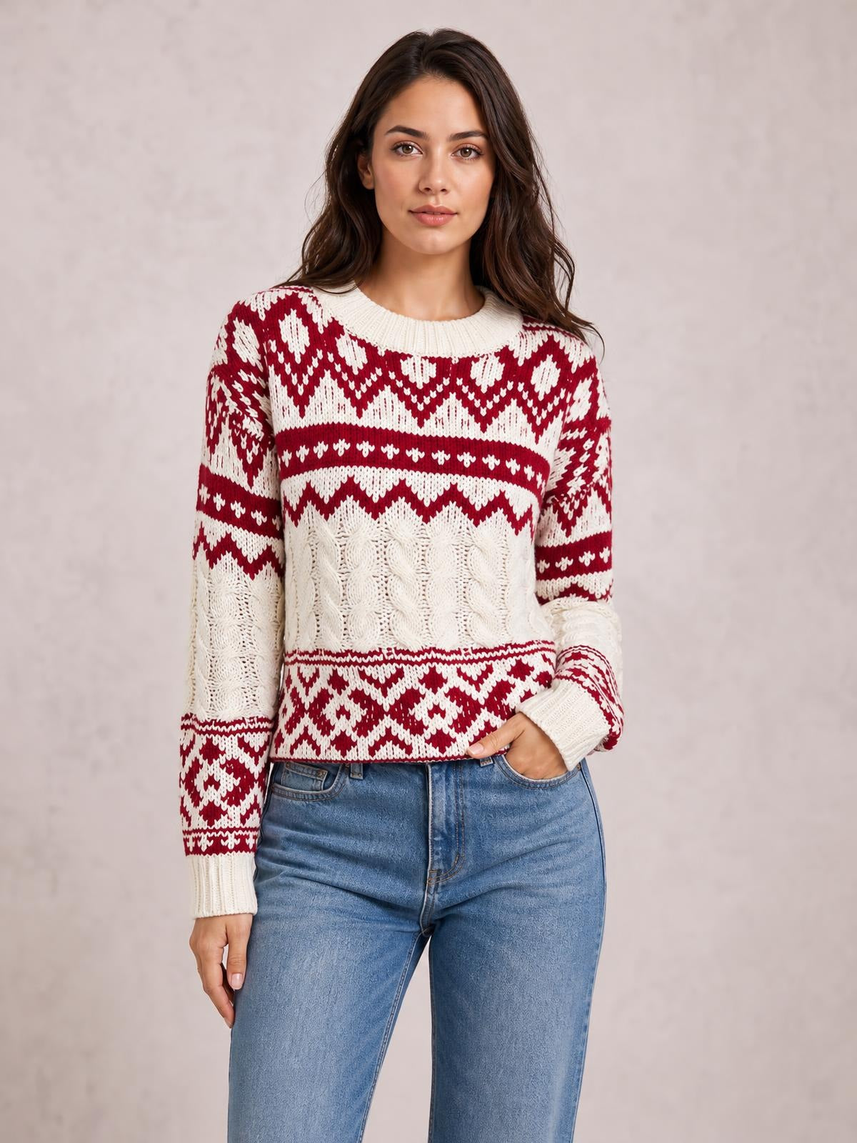 A woman stands in a red and cream Christmas cable knit sweater with long sleeves, a crew neck, ribbed trim, and a fitted waist-length silhouette.