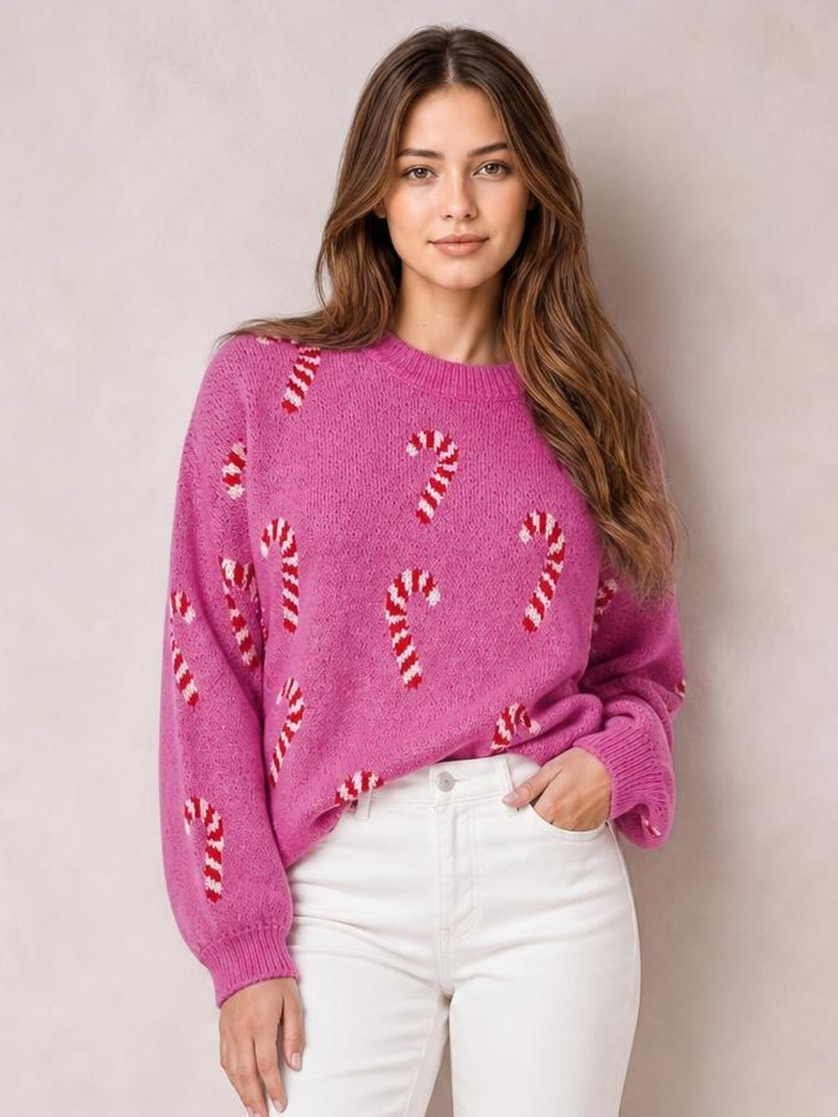 A model wears a pink drop-shoulder sweater with red-and-white candy cane motifs, a relaxed silhouette, crew neckline, and ribbed cuffs.