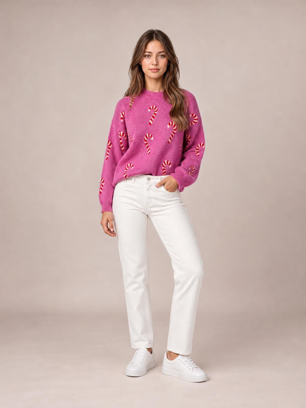 A model poses in a relaxed pink knit Christmas sweater with red-and-white candy cane motifs, crew neck, drop shoulders, ribbed cuffs and hem.