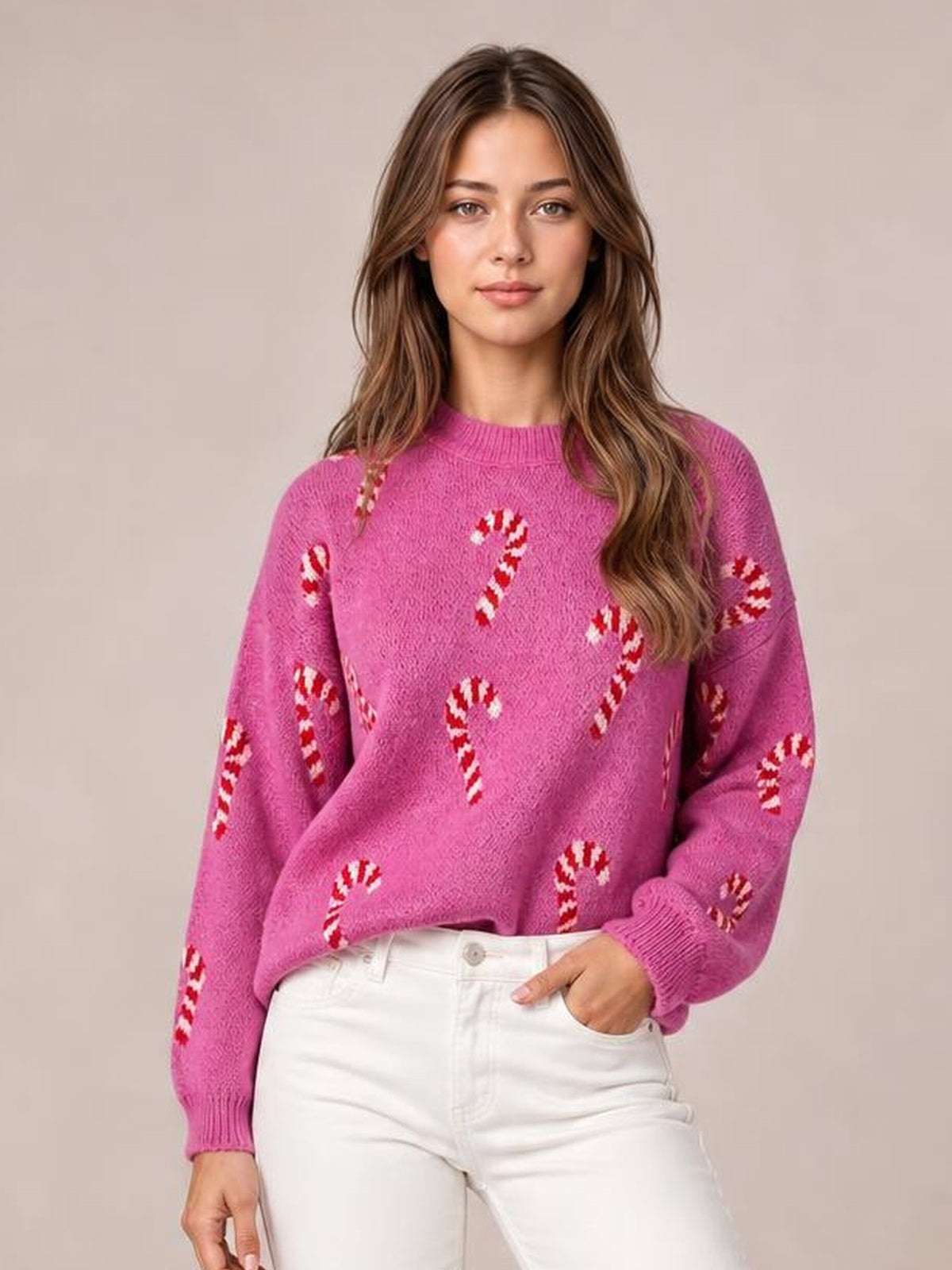 Model wears a pink Christmas sweater with red-and-white candy cane motifs, crew neck, drop shoulders, ribbed cuffs, and a relaxed silhouette.