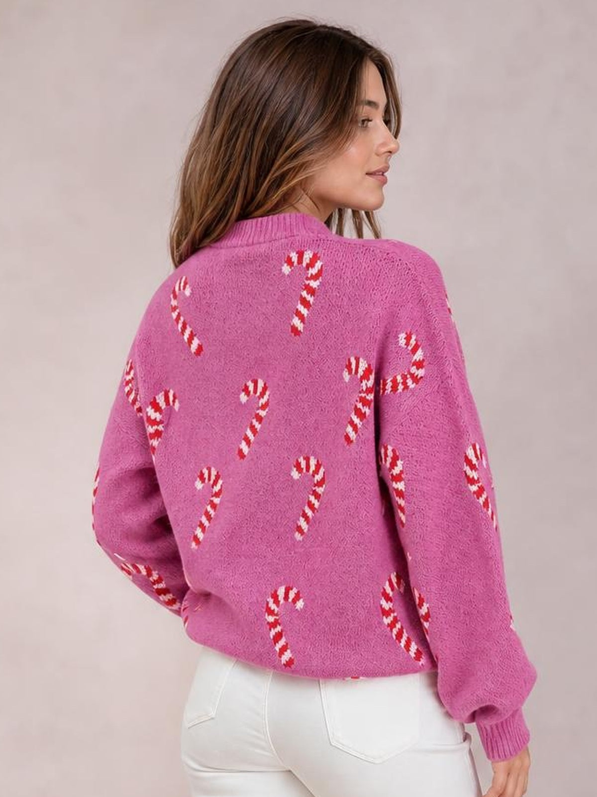 Model shown from behind in a pink Christmas sweater with candy cane motifs, drop shoulders, a relaxed silhouette, and ribbed collar, cuffs, and hem.