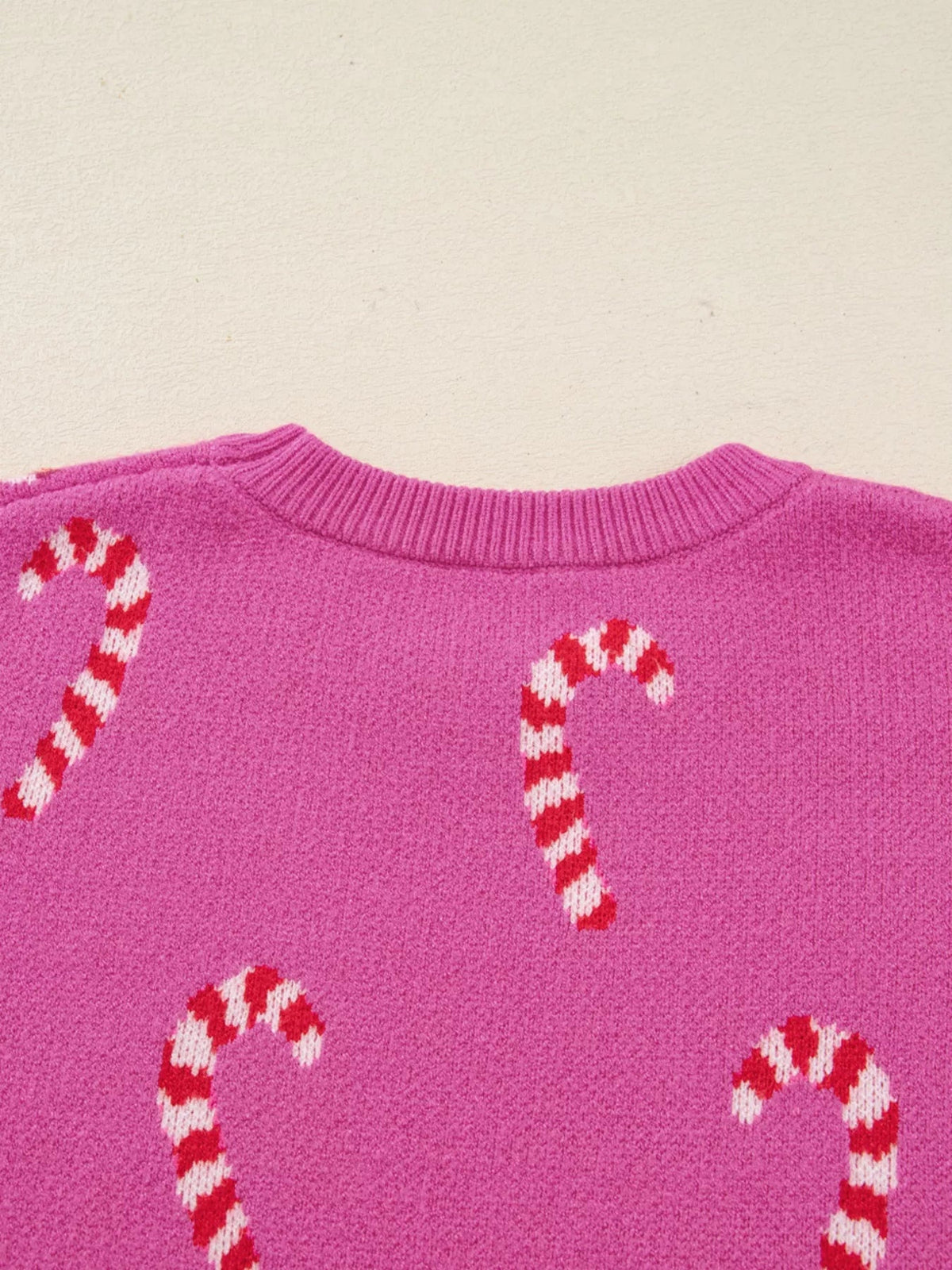 Close-up of a pink Christmas CanCane sweater featuring a ribbed crew neckline, relaxed drop-shoulder silhouette, and red-and-white candy cane motifs.