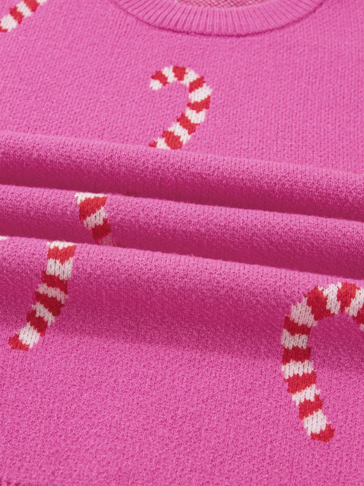 Close-up of a bright pink knit sweater with a ribbed crew neckline and red-and-white candy cane motifs, highlighting its soft textured construction.