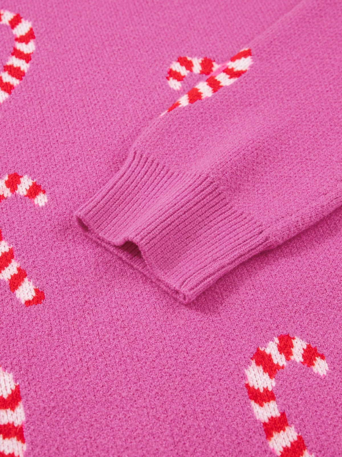 Close-up of a pink Christmas sweater featuring red-and-white candy cane motifs and a ribbed knit sleeve cuff.