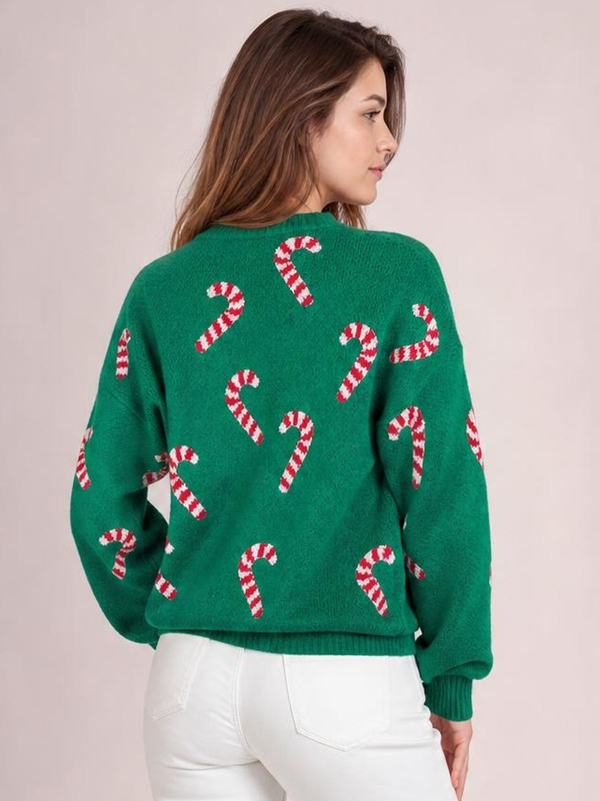 Model in a back-facing pose wears a green ribbed Christmas sweater with red-and-white candy cane print, drop shoulders, relaxed sleeves, and a ribbed hem.