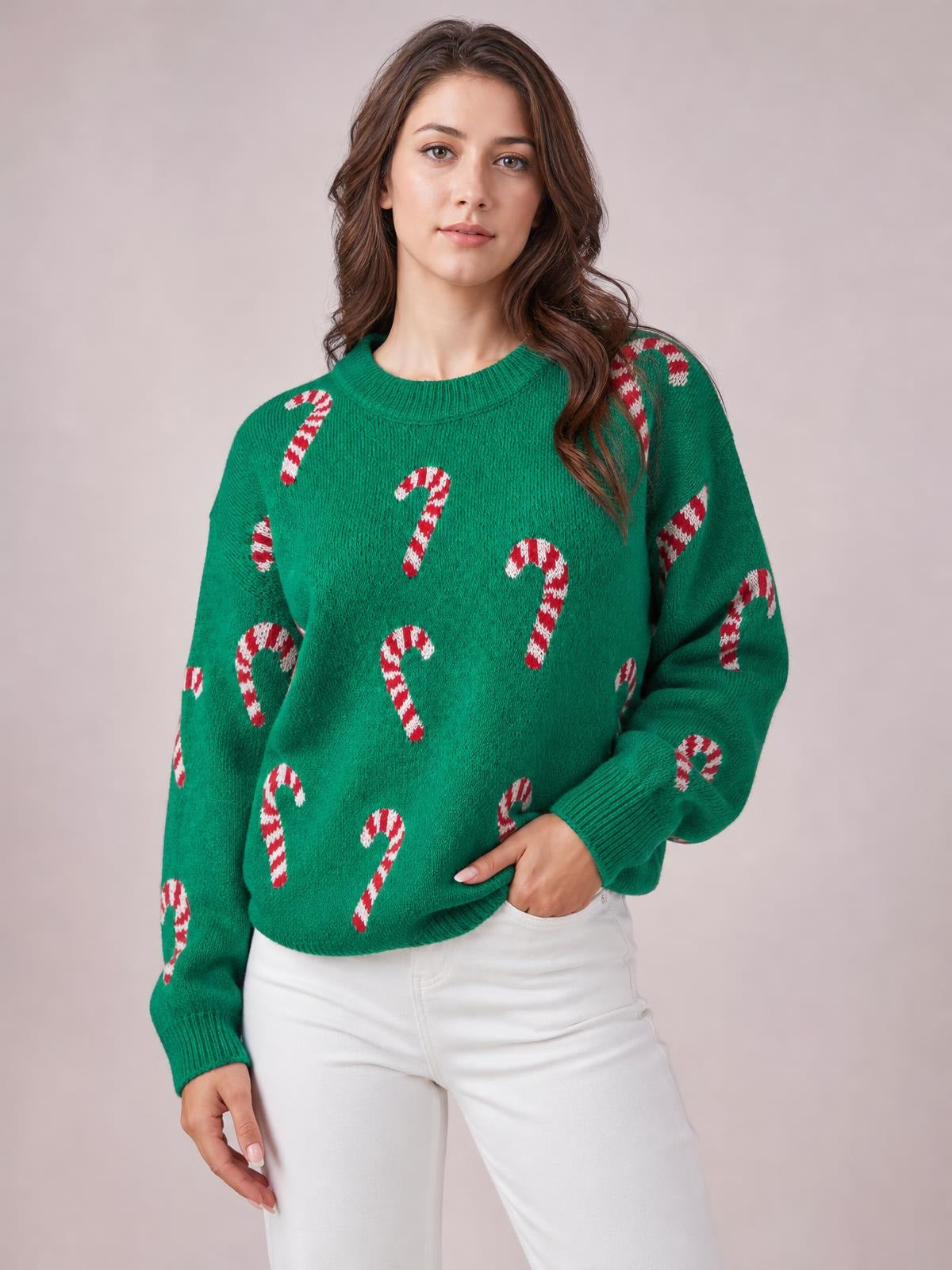 A model poses in a green Christmas sweater with red-and-white candy cane motifs, a relaxed drop-shoulder silhouette, ribbed crew neck, cuffs, and hem.