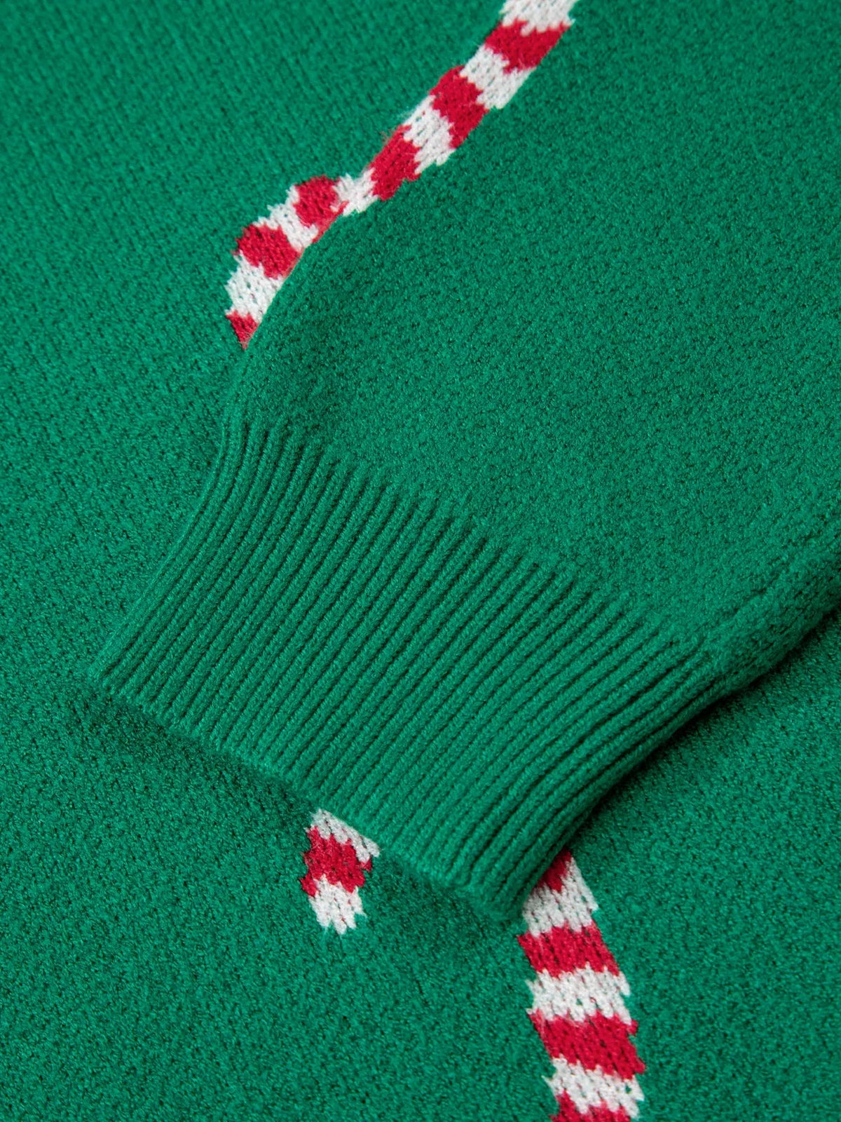 Close-up of a green ribbed Christmas sweater with red-and-white candy cane motifs and a folded ribbed cuff.