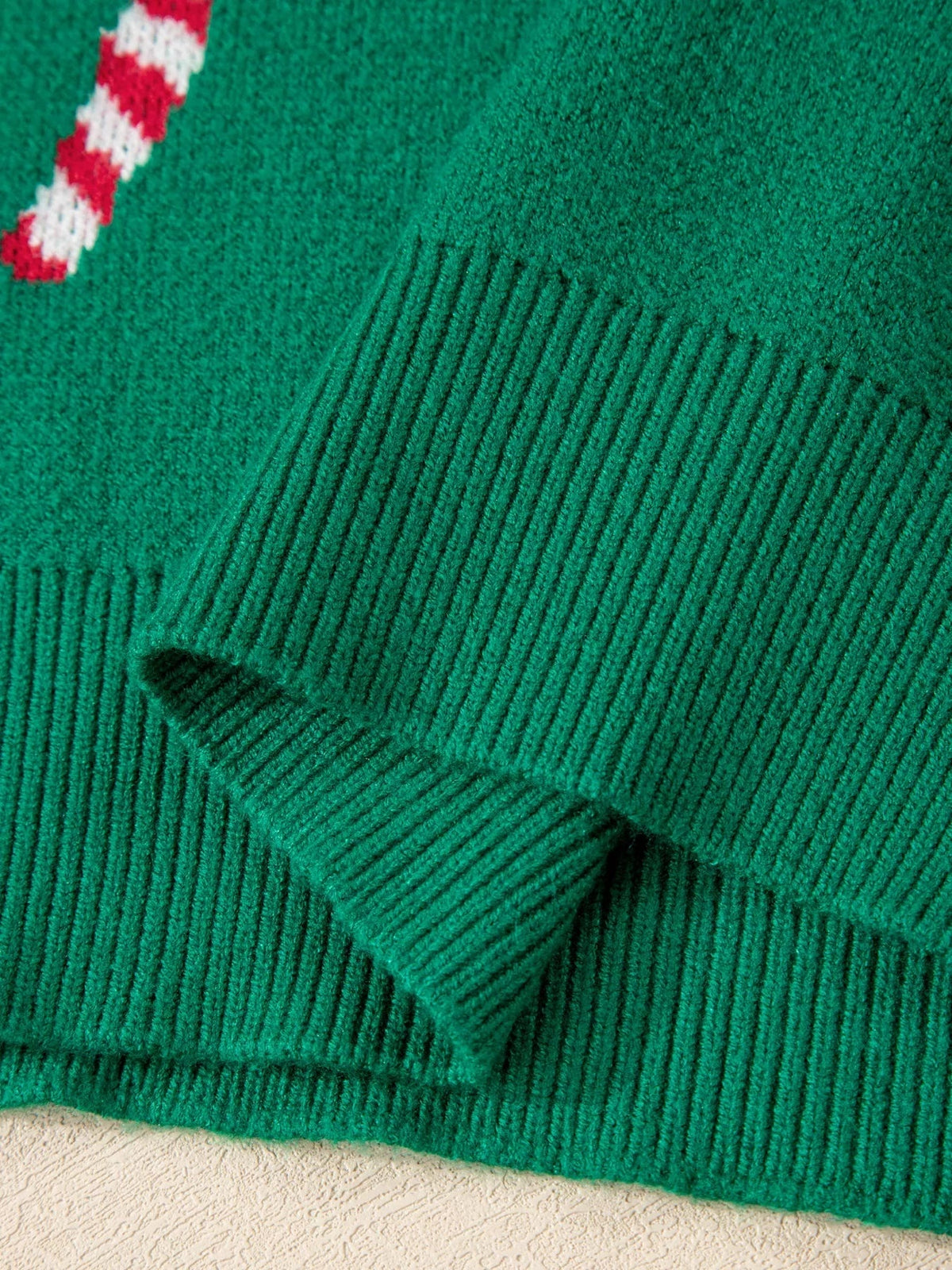 Close-up of a green ribbed Christmas sweater showing a drop-shoulder seam, textured knit construction, and partial red-and-white candy cane motif.