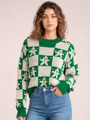 Model wears a green and cream Christmas checkerboard gingerbread sweater with a round neck, long sleeves, ribbed cuffs and hem, and a relaxed silhouette.