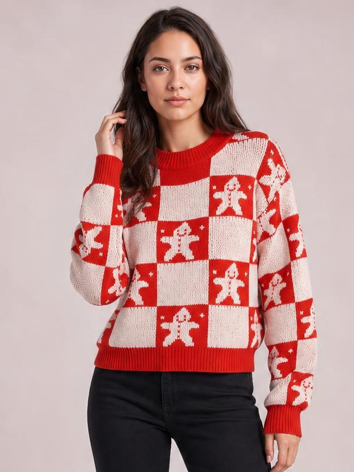 A model poses in a red and cream Christmas checkerboard gingerbread round-neck sweater with a relaxed silhouette, ribbed cuffs, collar, and hem.