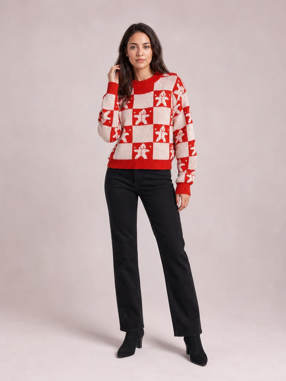 A model poses in a red and white Christmas checkerboard gingerbread sweater with a round neck, long sleeves, and ribbed cuffs and hem.