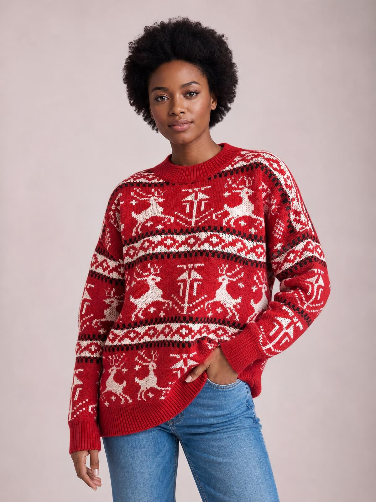 Model wearing a red Christmas sweater with a round neck, long sleeves, ribbed cuffs and hem, and white reindeer pattern, posing with one hand in her jeans pocket.