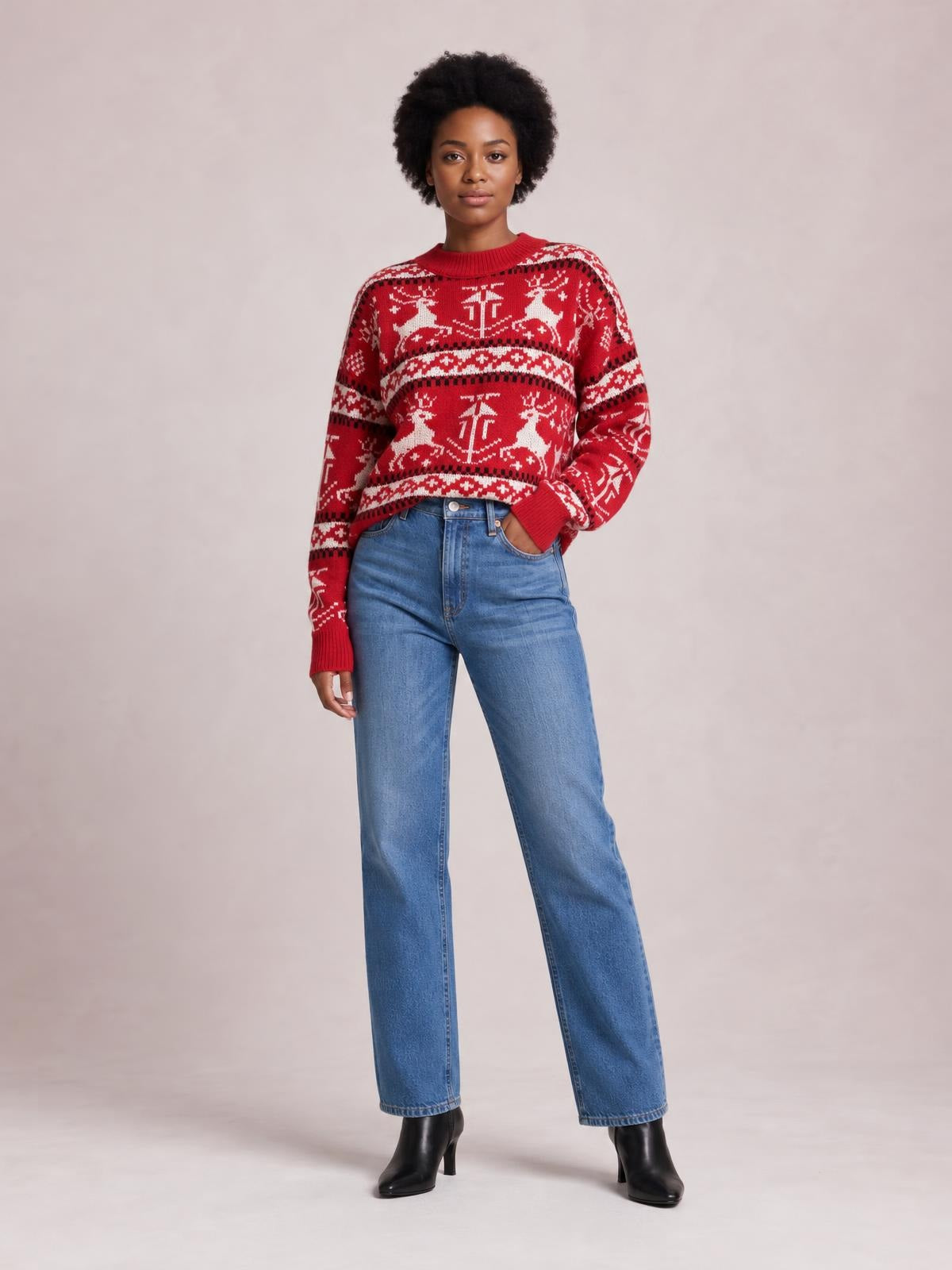 A model stands in a red Christmas sweater with a round neck, long sleeves, reindeer and snowflake motifs, striped bands, and a relaxed silhouette.