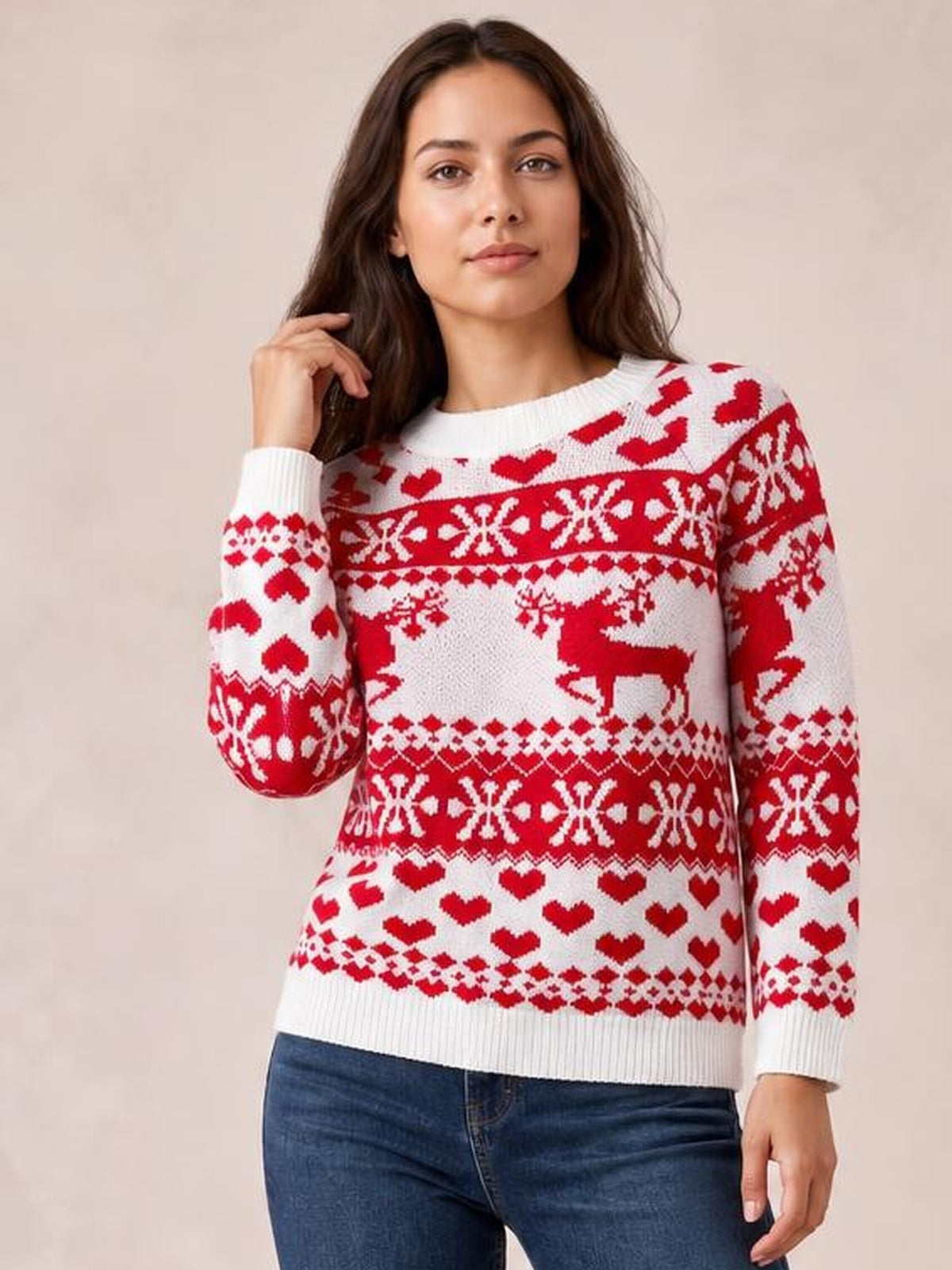 A model poses in a white Christmas sweater with red hearts, reindeer, and snowflake knit patterns, a round neck, long sleeves, and a fitted silhouette.