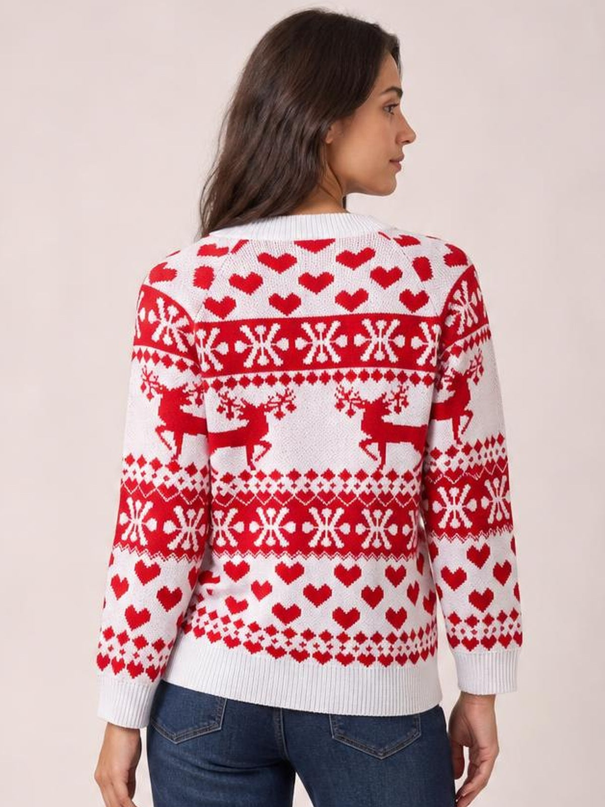 Model shown from the back wearing a white Christmas sweater with red hearts, reindeer, snowflakes, a round neck, long sleeves, and ribbed cuffs and hem.