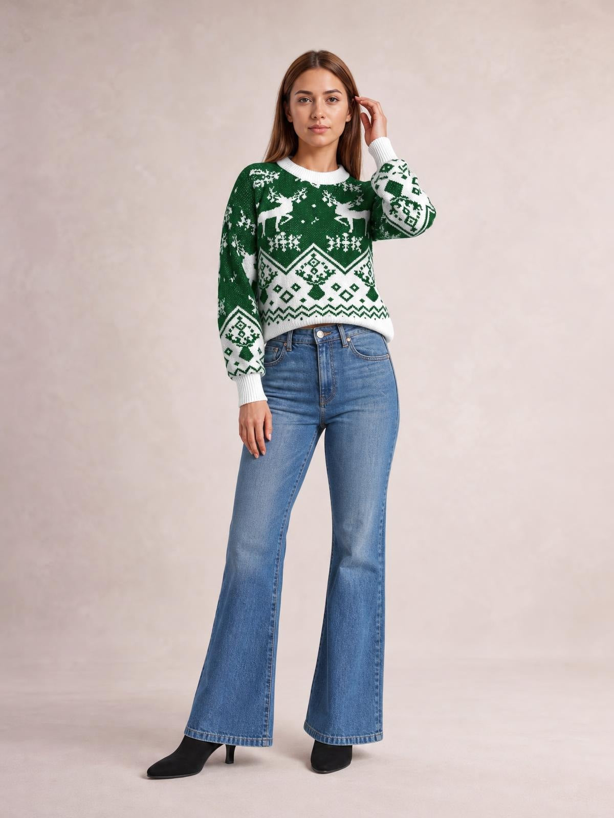 Model wears a green and white Christmas-patterned round-neck long-sleeve sweater with a relaxed silhouette, ribbed cuffs and hem, posing with one hand near her hair.