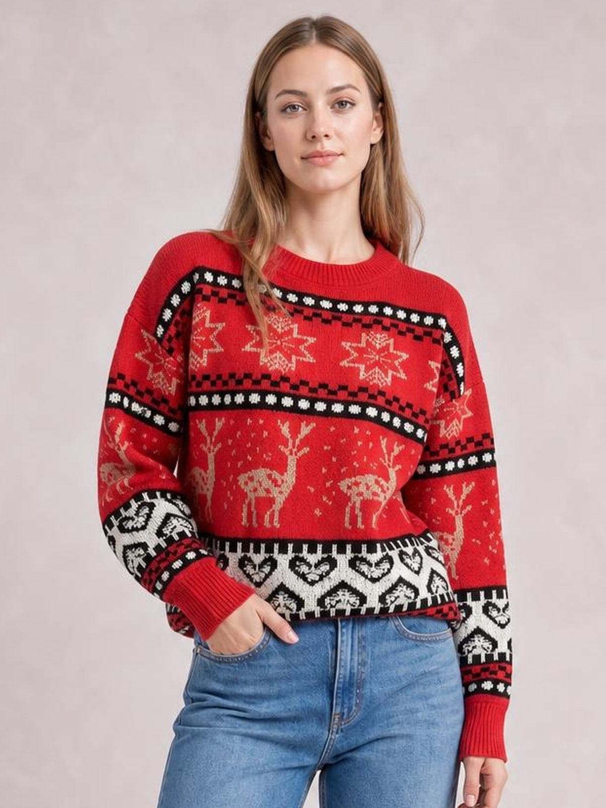 Model poses with one hand in her jeans pocket, wearing a red Christmas element round-neck sweater with long sleeves, festive snowflake, reindeer, and geometric knit patterns.