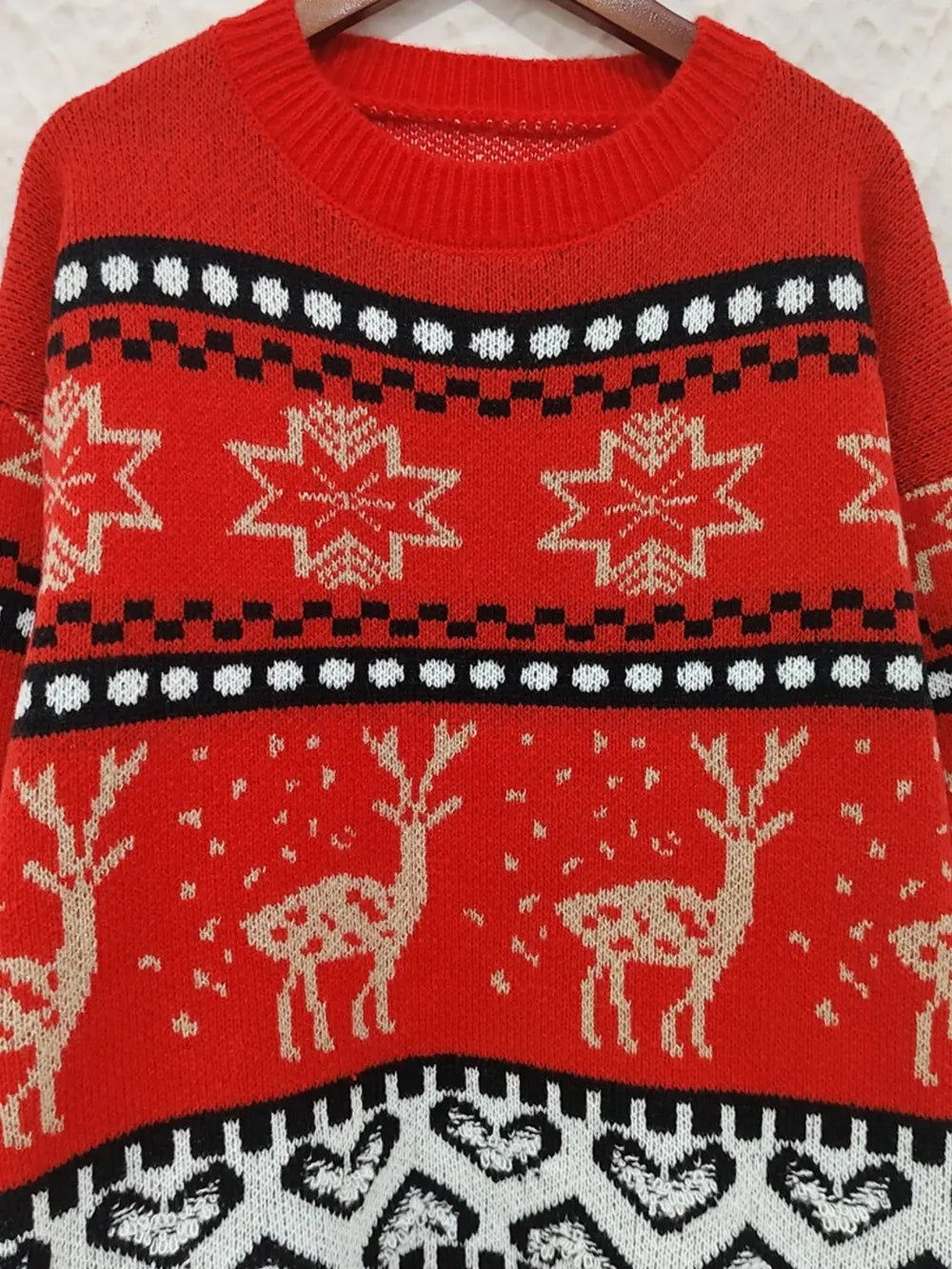 Red knit Christmas sweater with a ribbed round neck, long sleeves, and a festive patterned design featuring snowflakes, reindeer, and black-and-white bands.