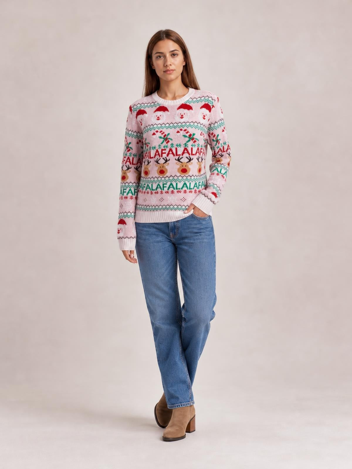 A model poses with one hand in her jeans pocket, wearing a pink Christmas round-neck sweater with long sleeves, festive Santa, reindeer and “FA LA LA” patterns, and ribbed trim.