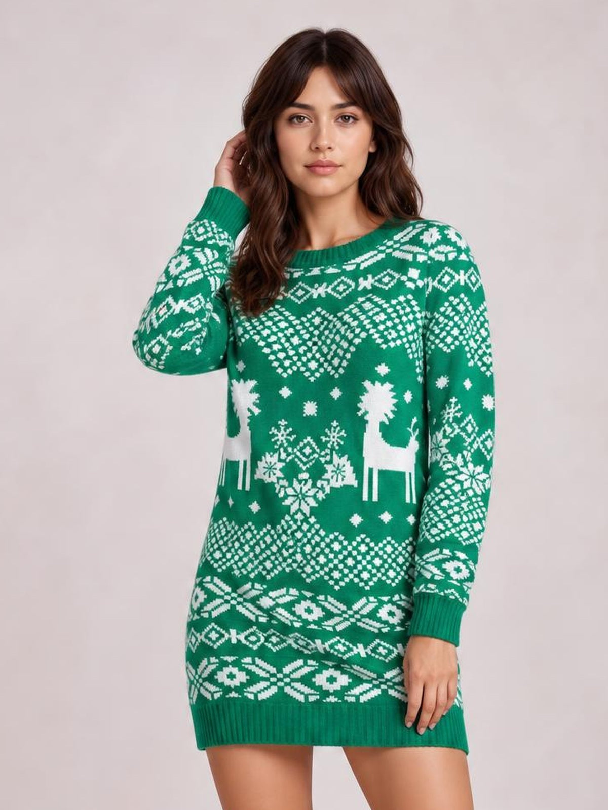 Model poses in a green Christmas sweater dress with a round neck, long sleeves, ribbed cuffs and hem, white reindeer and snowflake motifs, and a relaxed mini silhouette.