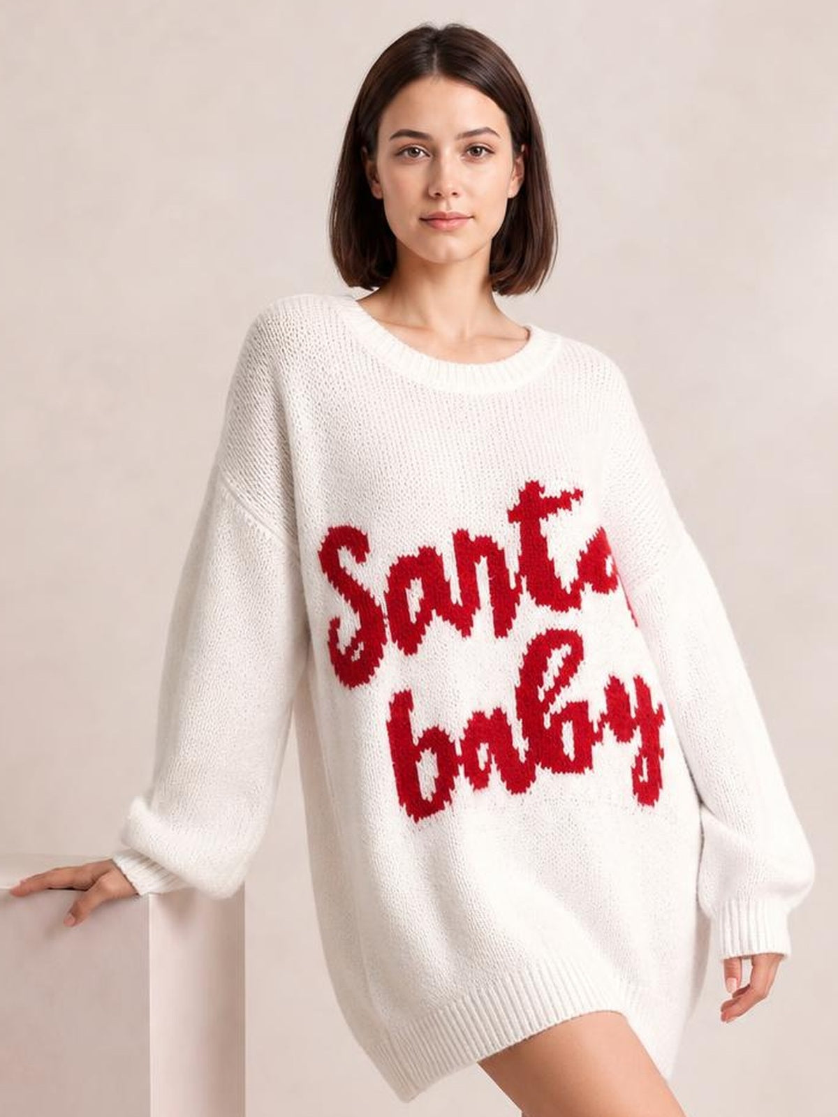 Model wears an oversized white Christmas letter sweater dress with red “Santa Baby” lettering, long sleeves, ribbed cuffs, crew neckline, and hem.