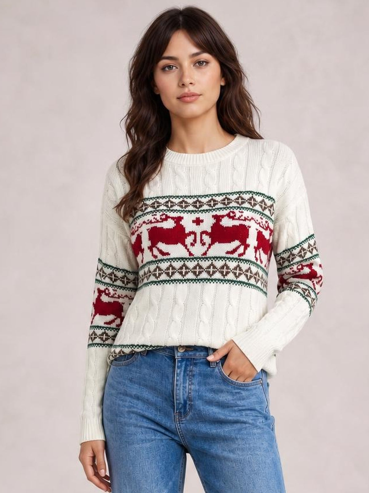 Model wearing a white cable-knit Christmas reindeer sweater with red and green patterned bands, crew neckline, long sleeves, and a relaxed silhouette.