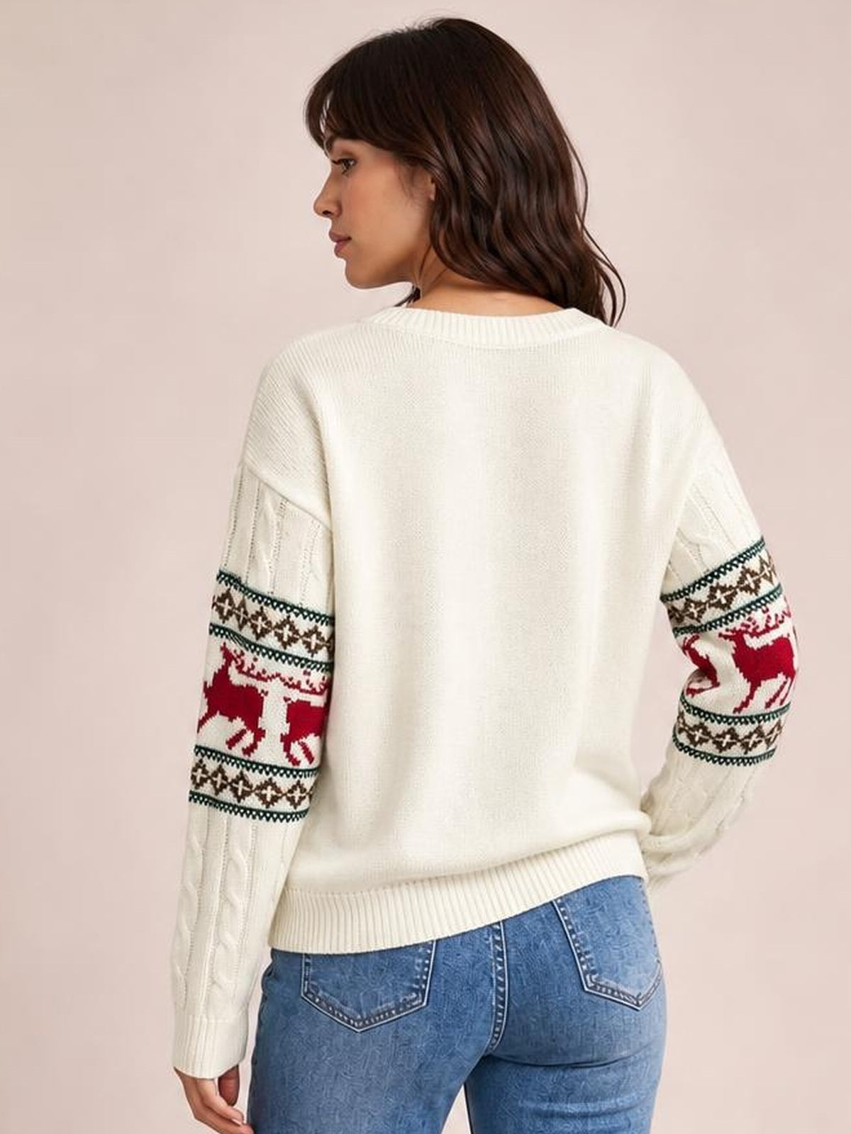 Model turned away displays a cream cable-knit Christmas sweater with ribbed trim, relaxed silhouette, and red reindeer and geometric patterned sleeves.