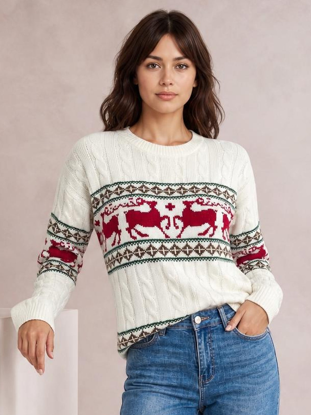 A woman poses in a white cable-knit Christmas sweater with red reindeer and patterned bands, ribbed crew neck, cuffs, and hem.