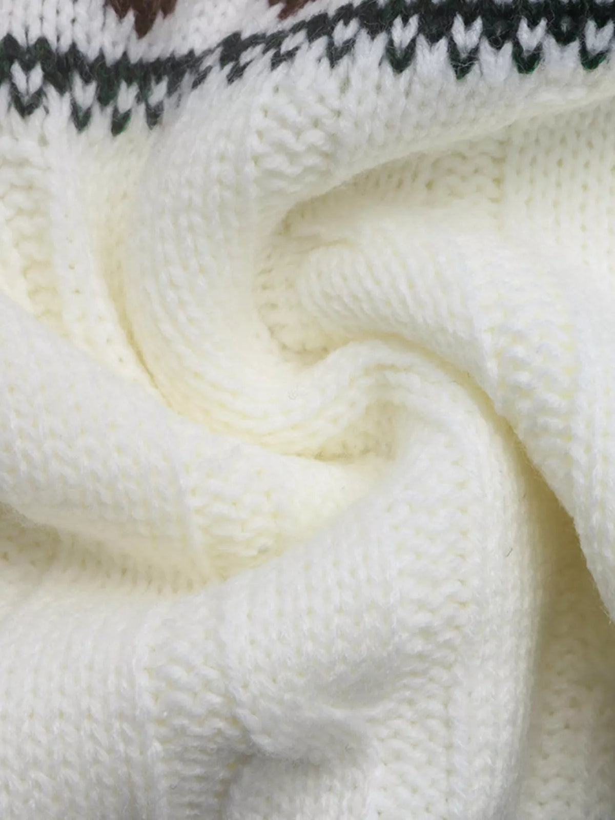 Close-up of a cream cable-knit sweater showing its soft textured acrylic knit construction and dark patterned trim near the upper edge.