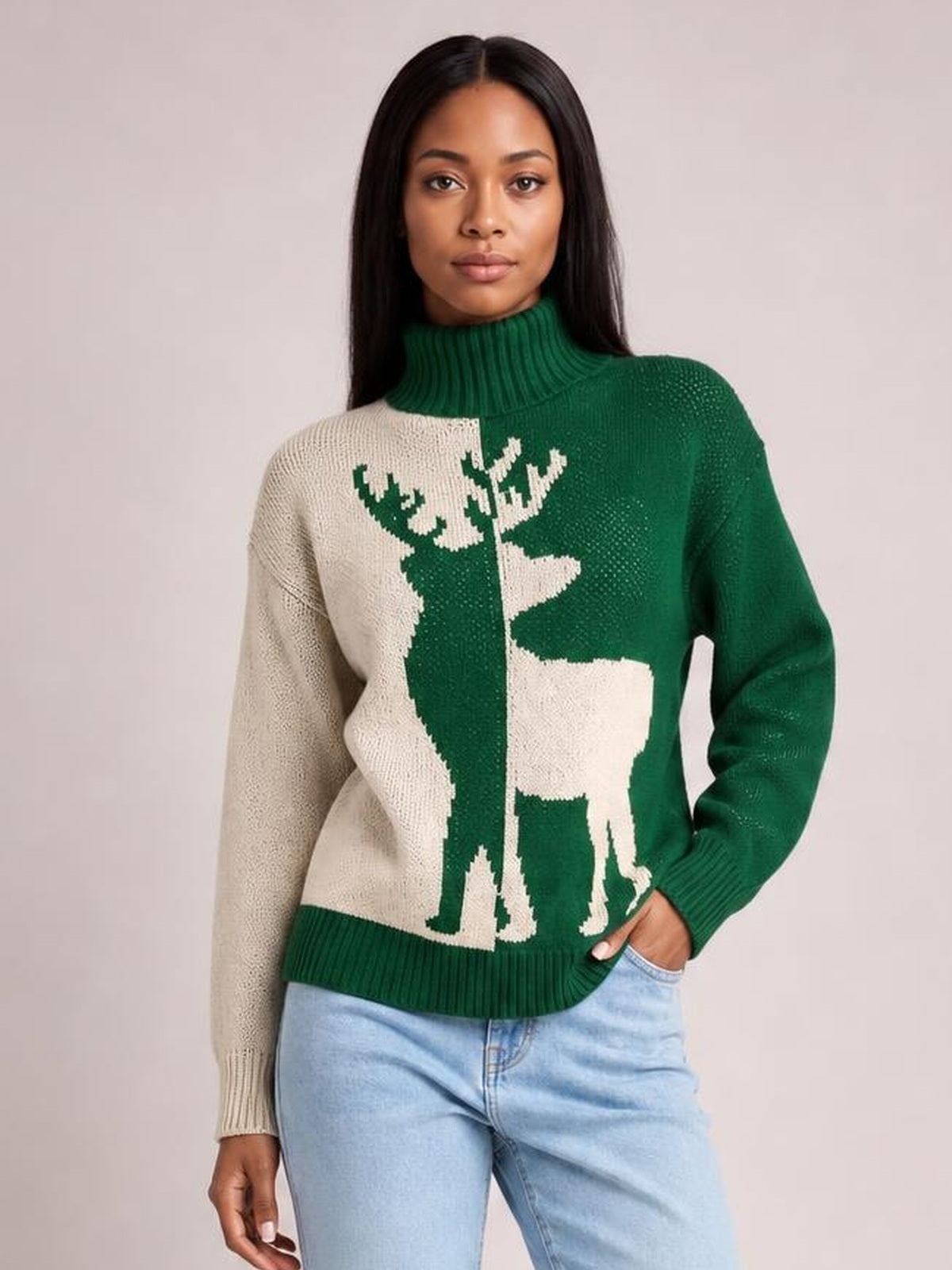 Model poses with one hand in her pocket wearing a green and cream Christmas reindeer turtleneck sweater with ribbed cuffs, hem, and collar.