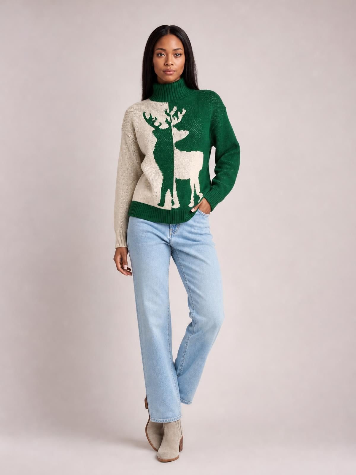 Model poses in a green and cream ribbed Christmas reindeer turtleneck sweater with a relaxed silhouette, one hand in her jeans pocket.