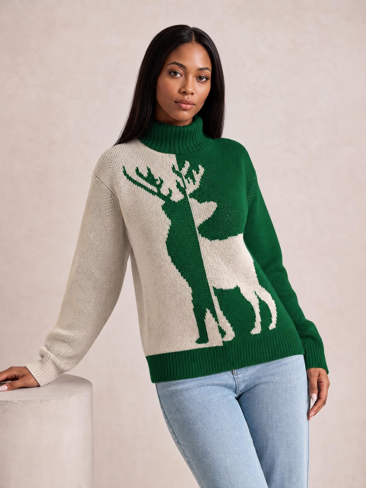 A woman leans against a pedestal wearing a green and cream ribbed turtleneck sweater with a large reindeer motif, long sleeves, and a relaxed silhouette.