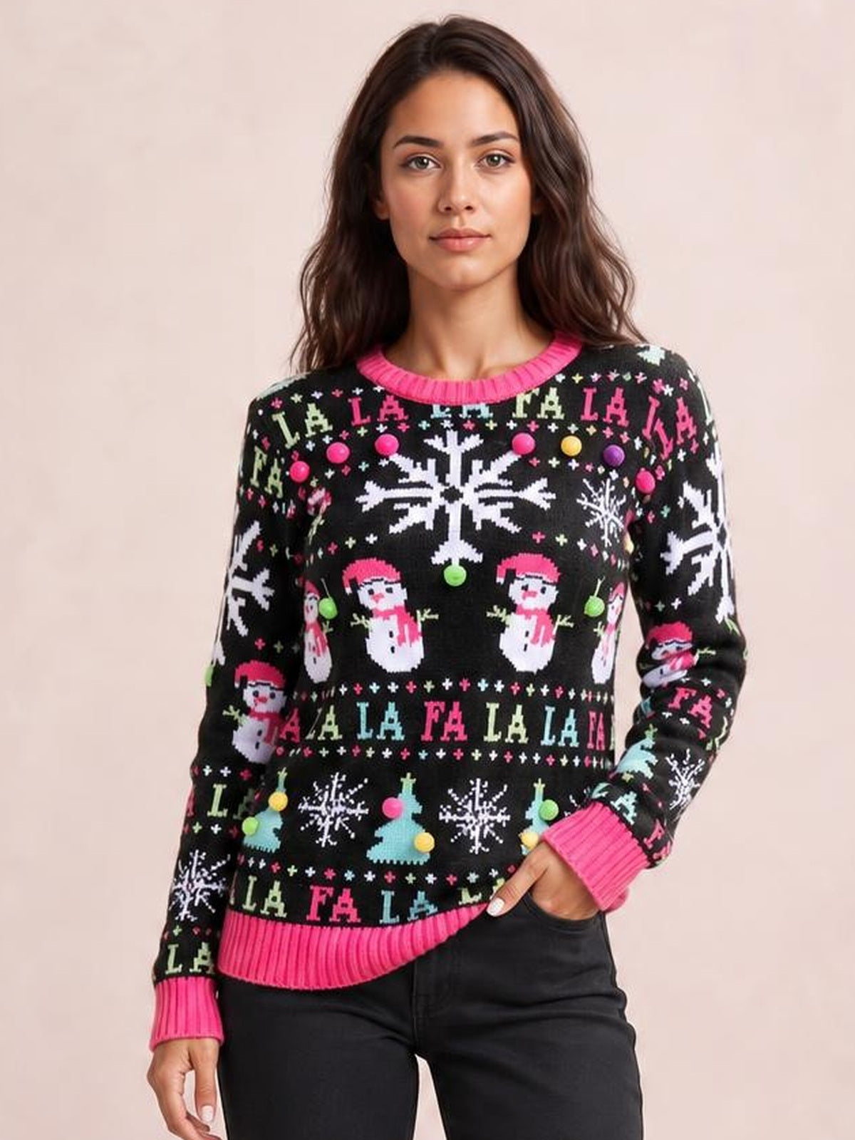 Model wears a black Christmas sweater with colorful snowflake and Santa motifs, long sleeves, bright pink ribbed trim, and a relaxed silhouette, posing with one hand in a pocket.