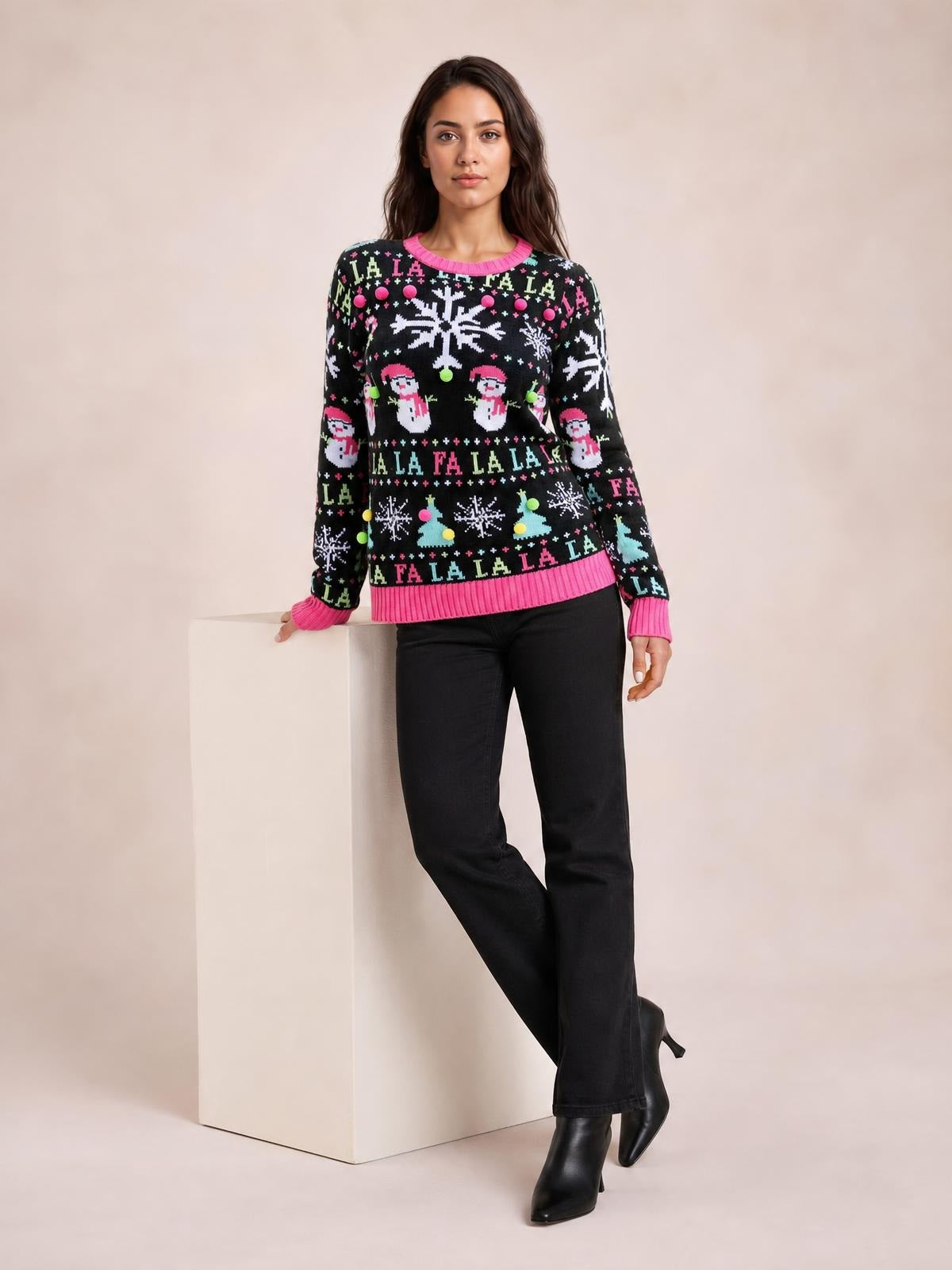 A model leans against a pedestal wearing a black Christmas sweater with pink ribbed crew neck, cuffs and hem, long sleeves, and festive snowflake and snowman motifs.