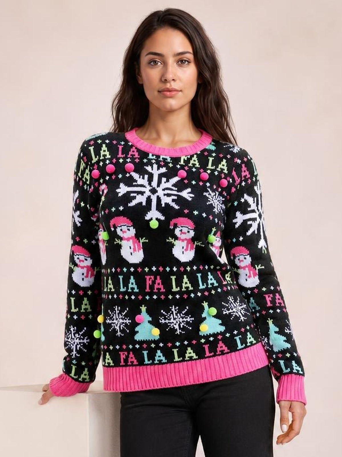 A model poses in a black Christmas sweater with colorful snowflake, Santa, tree, and “LA LA LA” patterns and bright pink ribbed trim at the neck, cuffs, and hem.