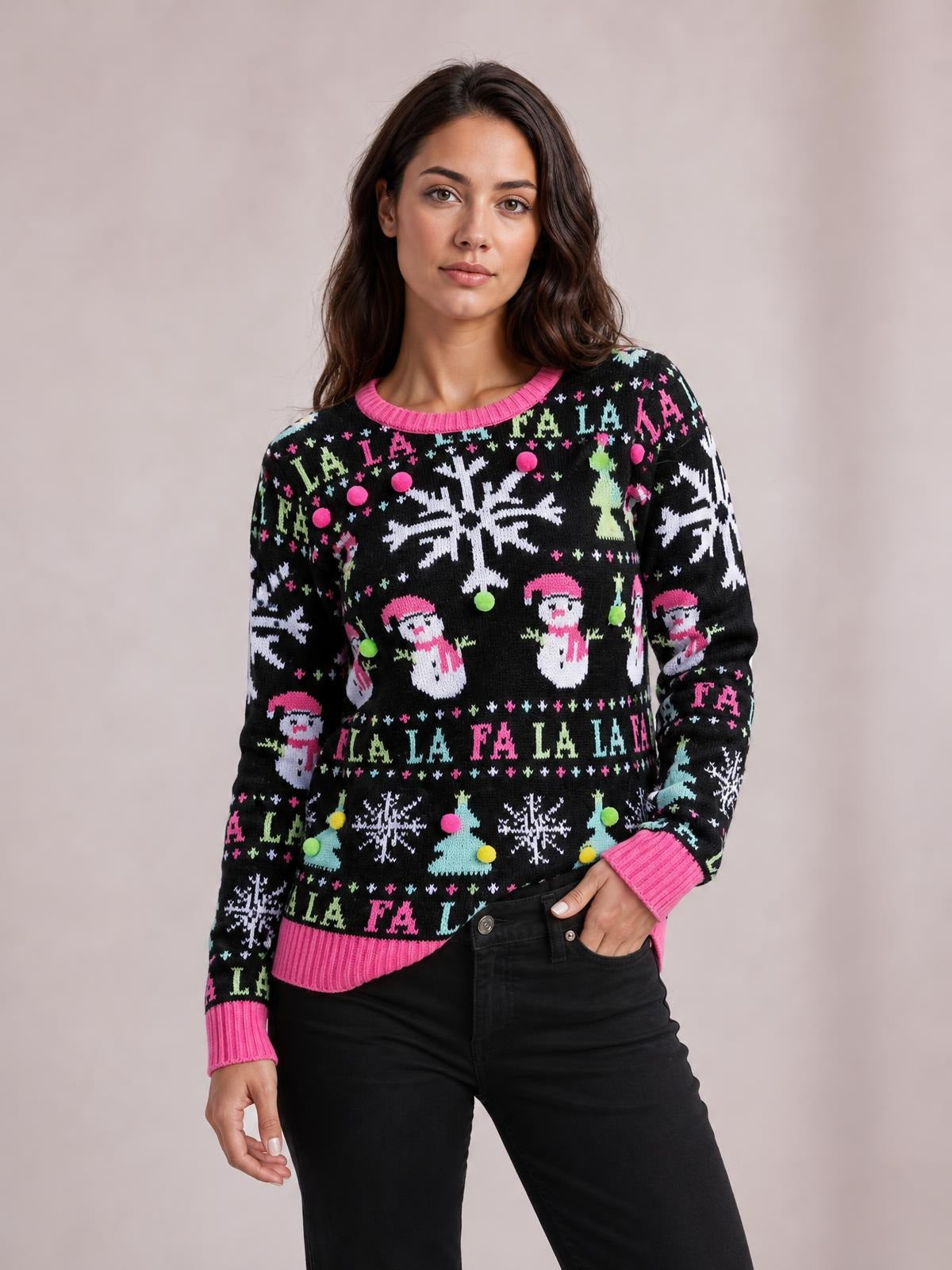Model poses in a black Christmas sweater with colorful snowflake, Santa, tree, and “FA LA LA” patterns, plus pink ribbed trim, crew neckline, cuffs, and hem.