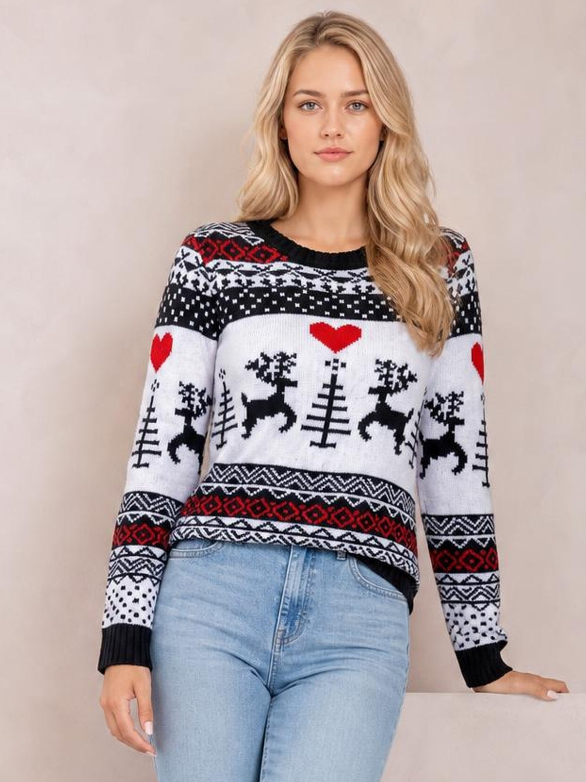 A woman wears a relaxed Christmas round neck sweater with black, white, and red reindeer, heart, and tree motifs, long sleeves, and ribbed cuffs.
