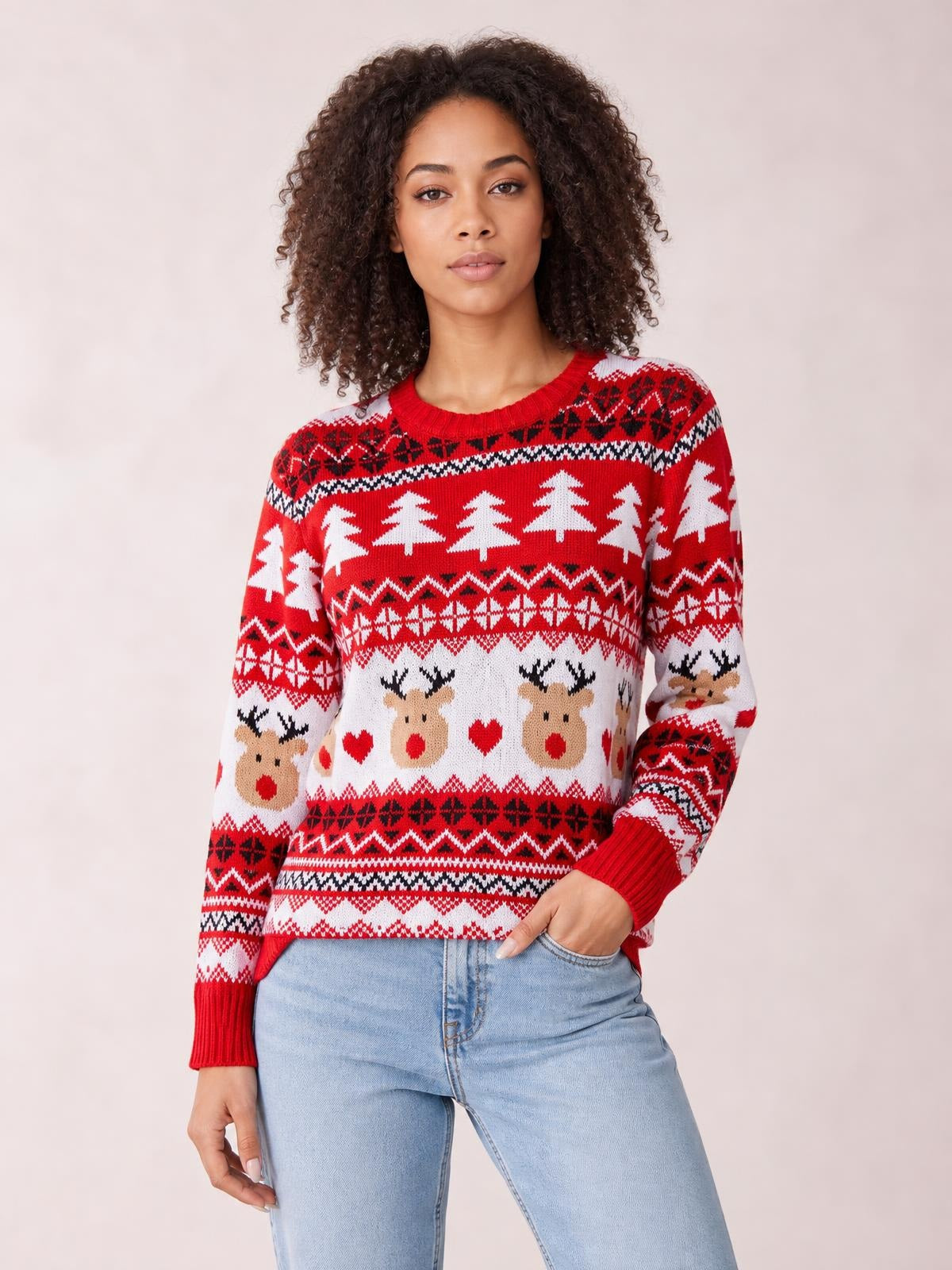 A model poses with one hand in her jeans pocket, wearing a red Christmas round neck sweater with long sleeves, ribbed cuffs, and festive reindeer and tree patterns.
