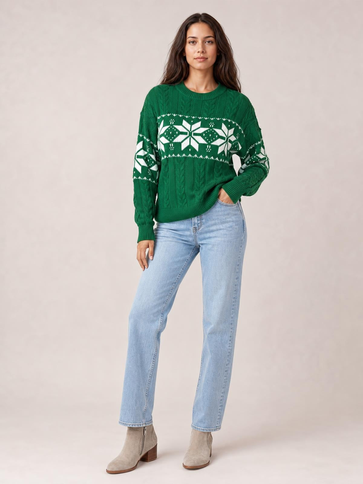 A model wears a green Christmas snowflake cable-knit sweater with a relaxed silhouette, crew neck, ribbed cuffs and hem, posing with one hand in her jeans pocket.