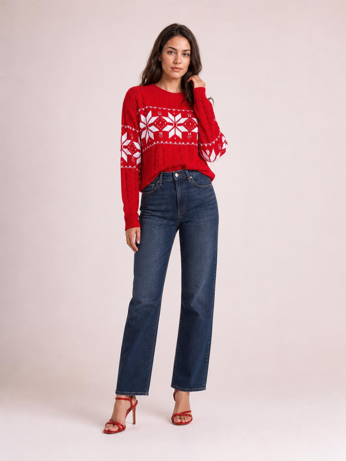 Model wearing a red Christmas snowflake cable knit sweater with long sleeves, ribbed trim, and a relaxed silhouette, posing with one hand near her hair.